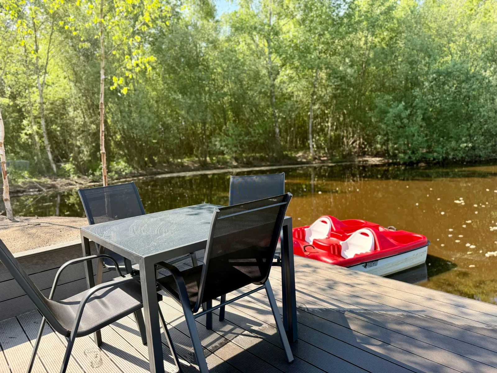 Terrasse am Wasser mit Tisch, Stühlen und rotem Tretboot
