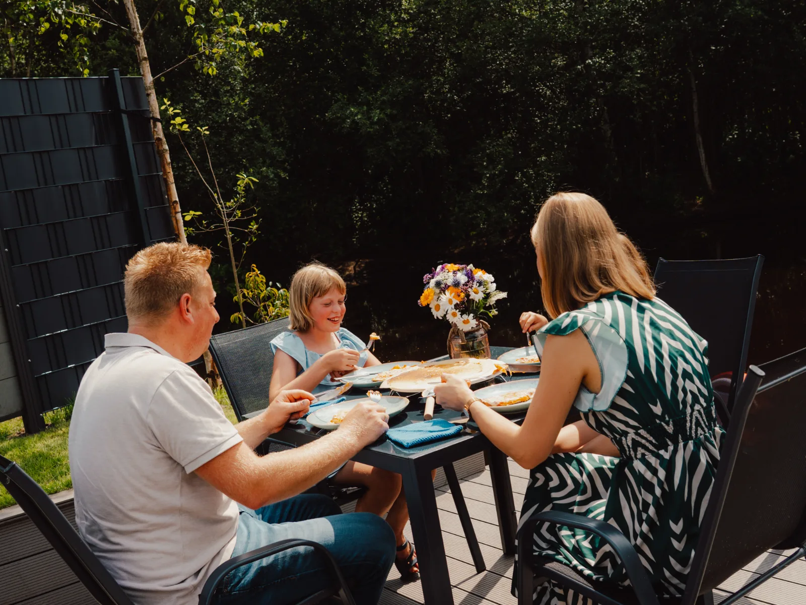 Familie sitzt zusammen am gedeckten Tisch auf der Terrasse