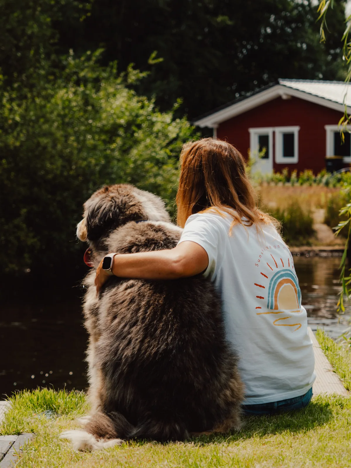 Frau trägt ihren Hund auf dem Arm am Seeufer